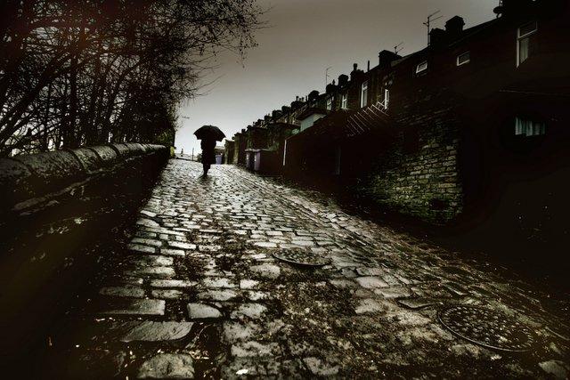 As the rain keeps coming, these glistening setts provide an historic backdrop as a man battles up a snicket in the Mill Town area of Skipton.
