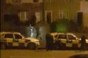 A person leaves a house in Canterbury, Bradford, watched by armed police