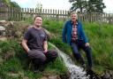 Jamie McEwan and Mark Corner by the water as it rejoins Backstone Gill after having gone through the new hydropower turbine