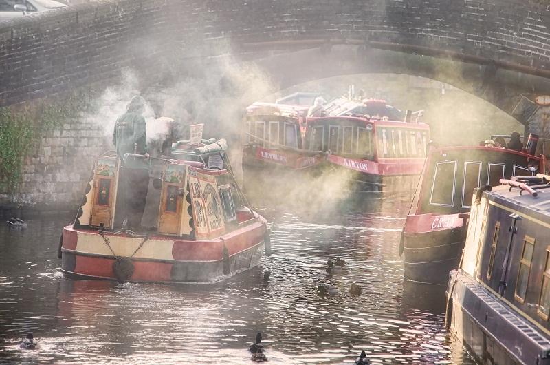 Smoke rises from a barge as it passes under a bridge in the early morning light on Springs Canal, Skipton
