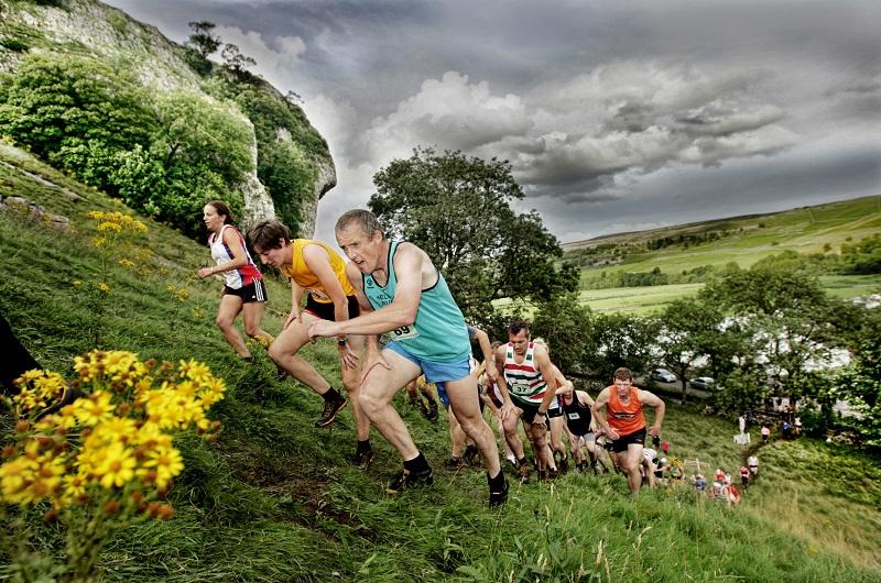 The crouched  figures of senior fell race competitors are pictured fighting the ascent in the classic Kilnsey Fell race with the majestic Crag in the background
