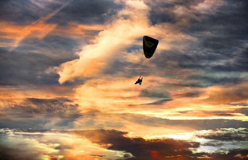 A powered paraglider soars through the sky, standing out against  the dramatic sunset west of Skipton