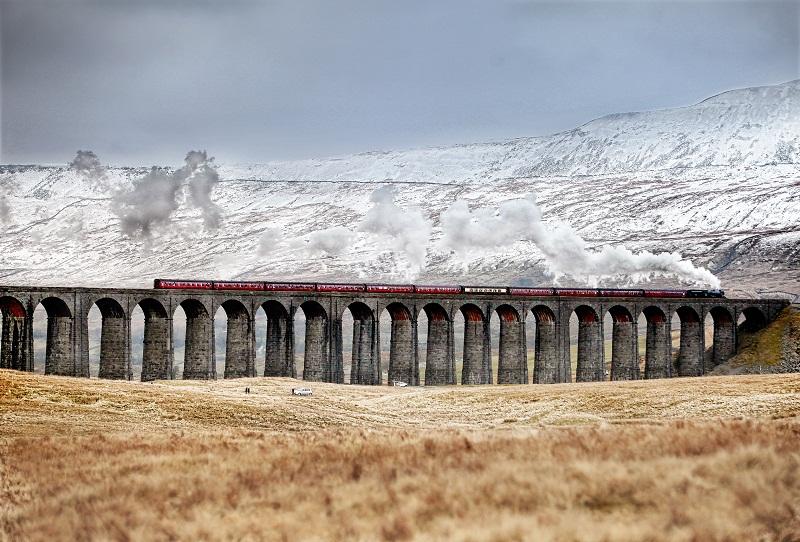 Set against a backdrop of snow-capped  fells, a steam train pulls across the majestic Ribblehead viaduct. 
