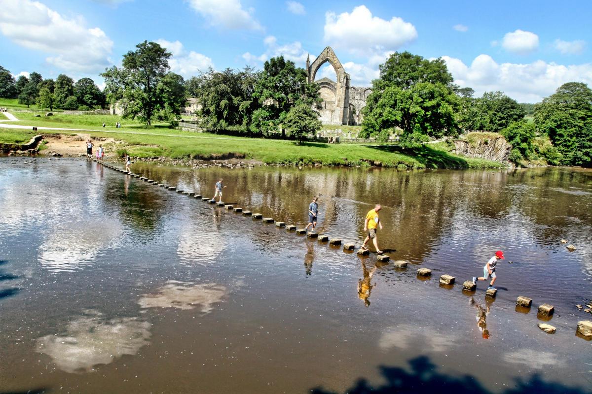 Visitors cross the ancient stepping stones at Bolton Priory.